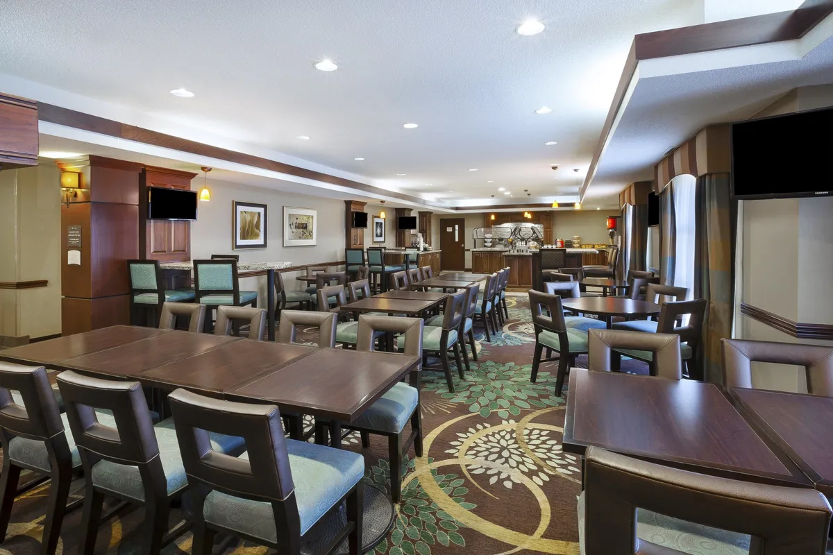 This image displays a dining area with tables arranged for meals, a decorative carpet, and a view of a bar area in the background. The mood is welcoming and relaxed, ideal for shared meals, casual gatherings, and comfortable dining experiences.