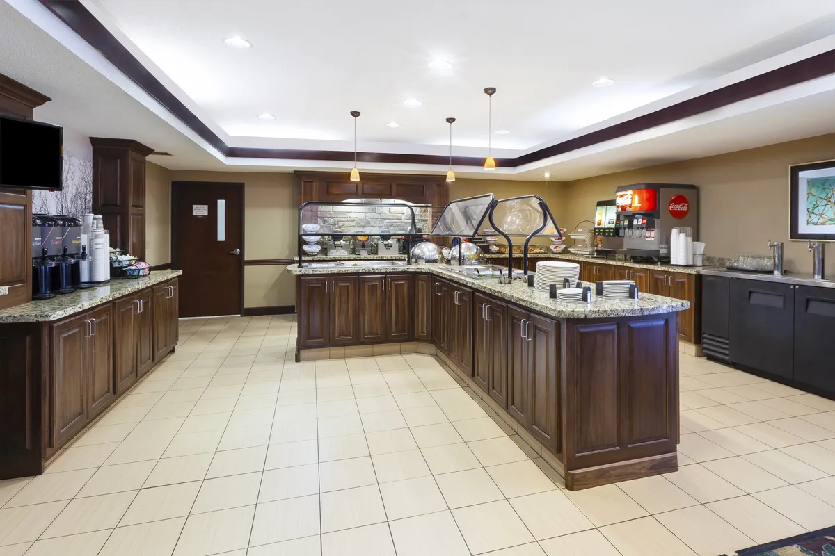 This image features a buffet counter with a dedicated coffee station, beverage dispenser, and decorative wall art. The area is inviting and communal, encouraging guests to enjoy breakfast and socialize while helping themselves to food and drinks. The coffee machine is prominently displayed, aligning with the mention of morning routines in the section.