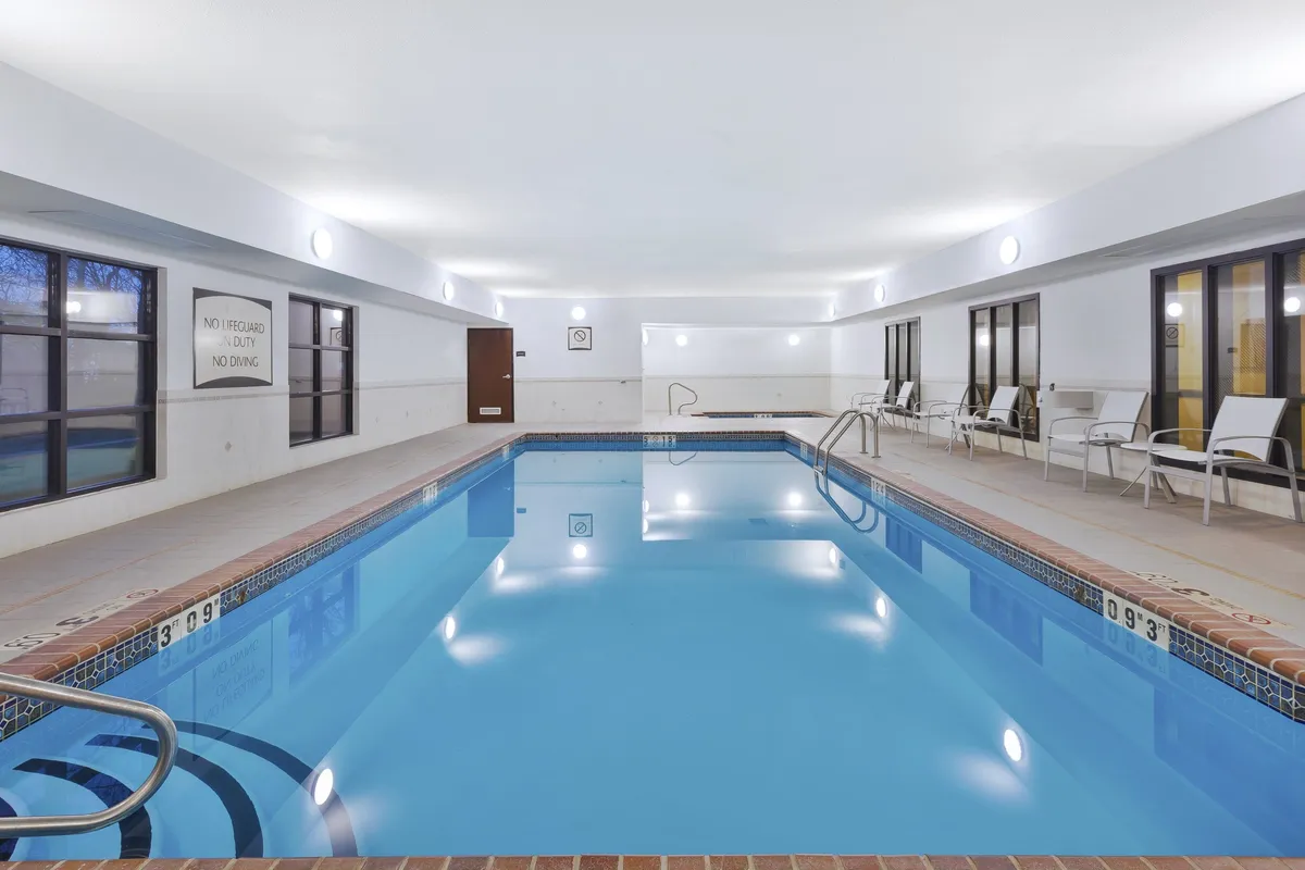 This image showcases an inviting indoor swimming pool bathed in soft lighting, with lounge chairs arranged alongside large windows. The tranquil atmosphere and subtle reflections on the water create a sense of retreat and relaxation, perfectly matching the section's focus on wellness amenities.