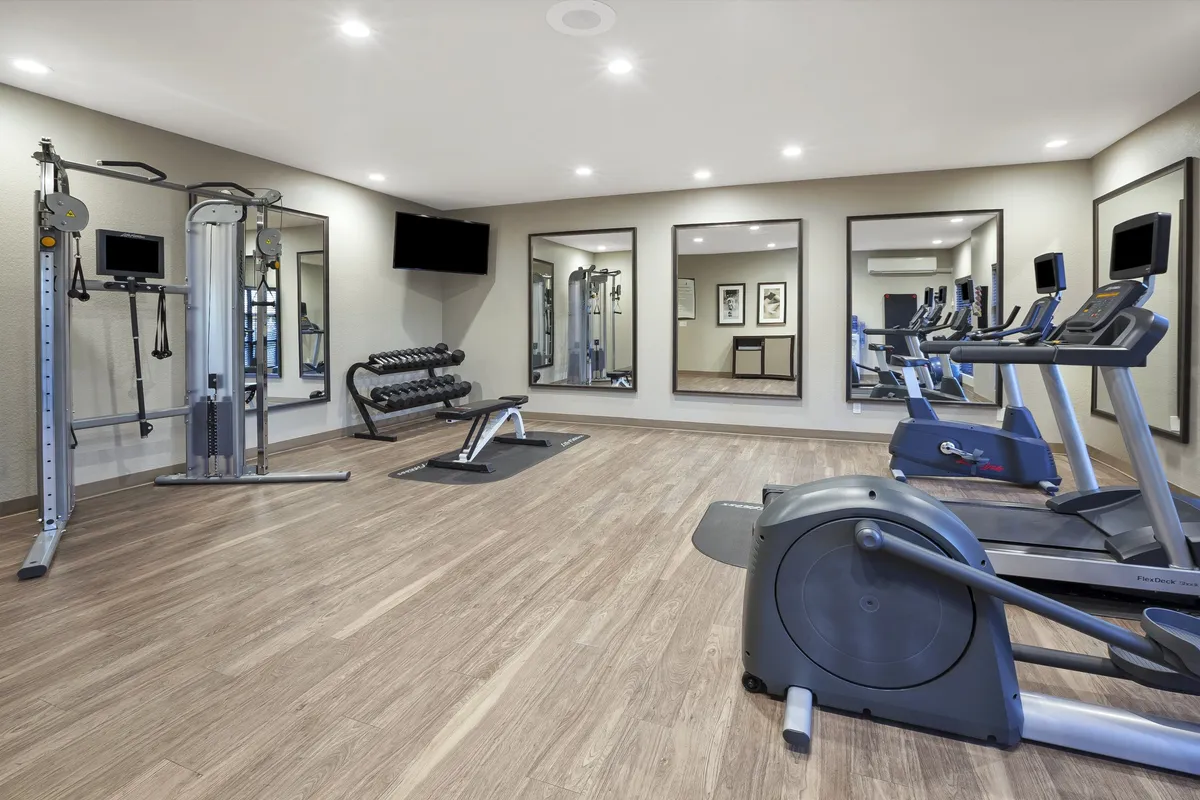 A modern fitness center equipped with various fitness machines, free weights, and mirrors. The space is well-lit and designed to encourage personal fitness milestones, group workouts, or solo training, aligning with the section's invitation to maintain wellness routines.