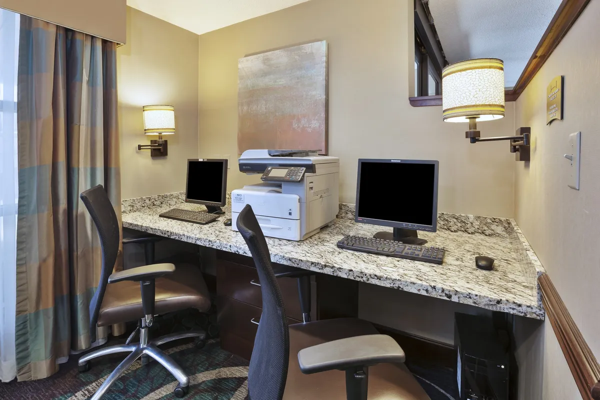 Two computer workstations with a printer, all set on a granite countertop, accompanied by artwork on the wall. The setup is inviting for both solo and collaborative work, emphasizing a focused and productive mood.
