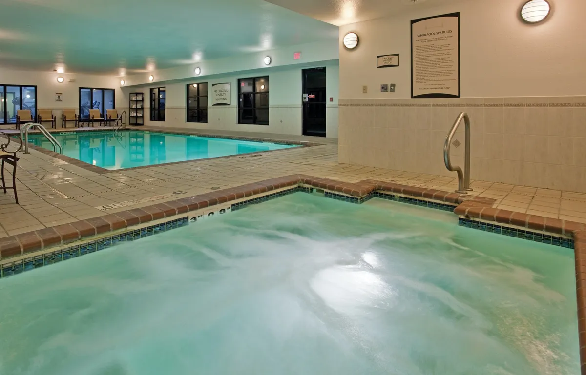 This scene features both the inviting hot tub and the adjacent indoor pool, surrounded by lounge chairs and enhanced by sophisticated lighting fixtures. The mood is serene and intimate, perfectly capturing the idea of a soothing retreat after a busy day.