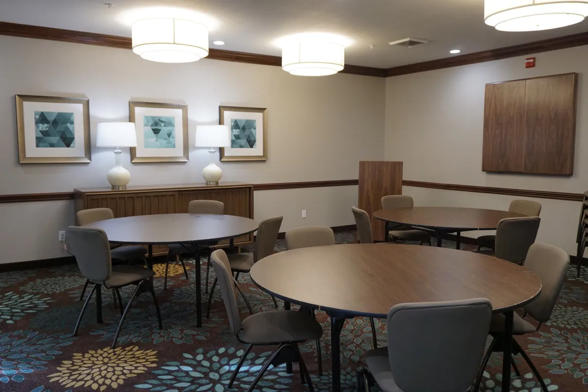 A stylish communal space with round tables, decorative lamps, and geometric artwork. The ambiance is inviting and ideal for casual gatherings or sipping wine, evoking a sense of connection and leisure.