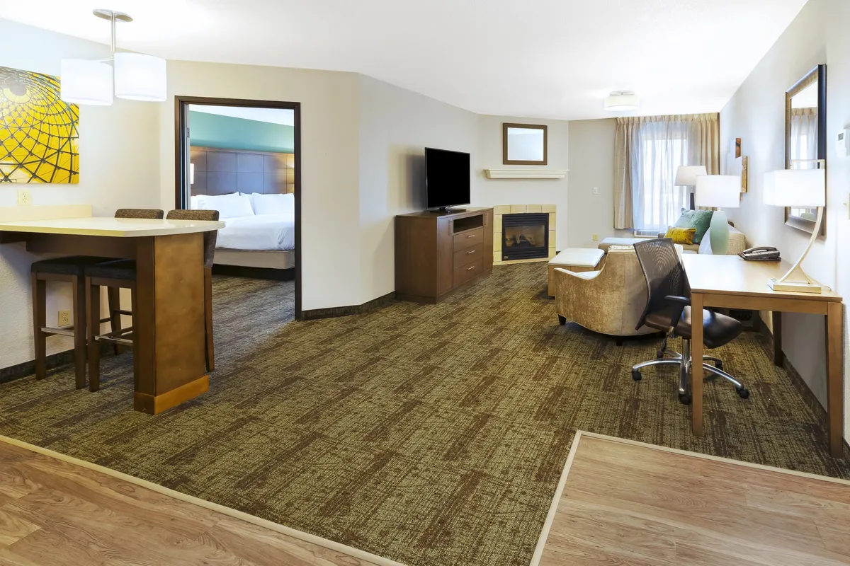 A comfortable living area featuring a cozy seating arrangement, fireplace, television, bar counter, and a work desk. The space is designed for both relaxation and productivity, with inviting décor and ample light that creates a welcoming atmosphere.