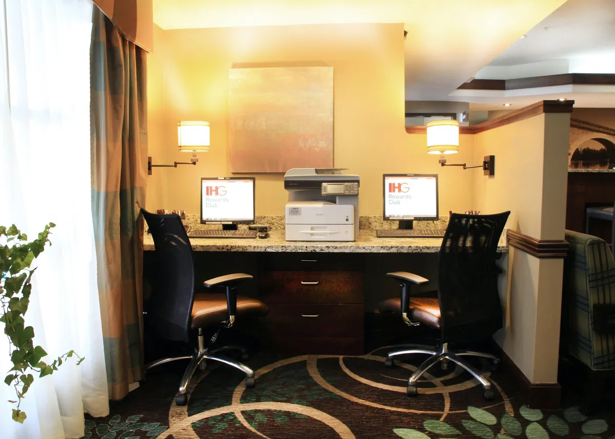 A well-lit business center featuring multiple computers, a printer, granite countertop, and tasteful artwork. The atmosphere is professional yet comfortable, providing an ideal environment for productivity and business tasks.