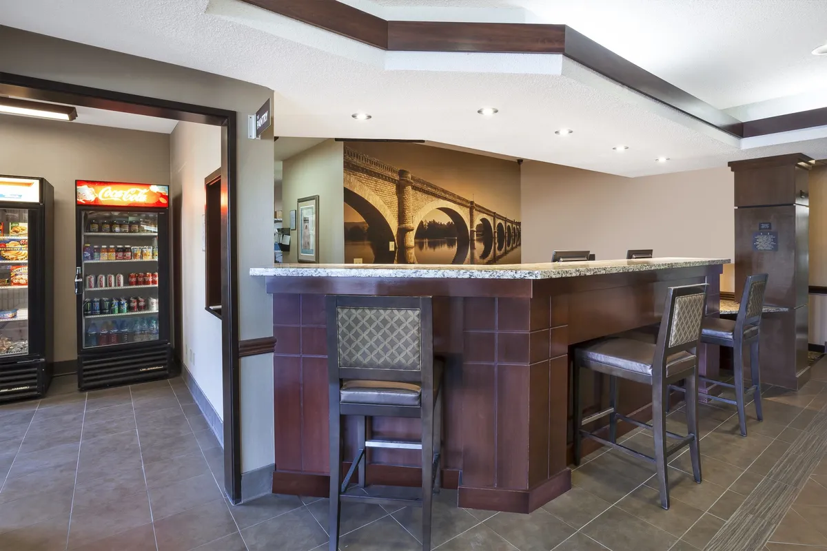 A welcoming lounge area featuring a modern bar counter, high stools, refrigerators, and decorative wall art. The space is designed for socializing, networking, and unwinding, making it ideal for evening guest receptions and informal gatherings.